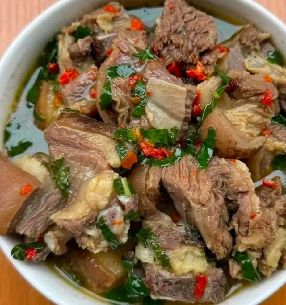 Bowl of spicy goat meat pepper soup with green herbs and red chili peppers.
